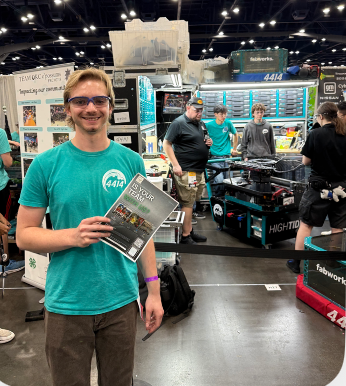 A FIRST Robotics participant holding a FlyerFly campaign flyer beside a competition robot